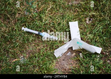 Gebrauchte Sicherheitsnadel, die von intravenösem Drogenkonsumenten im Stadtparkgras entsorgt wurde Stockfoto