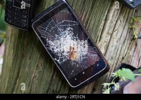 Alte Mobiltelefone sind an einen Kofferraum genagelt. Die stark beschädigten Mobiltelefone sind veraltet Stockfoto