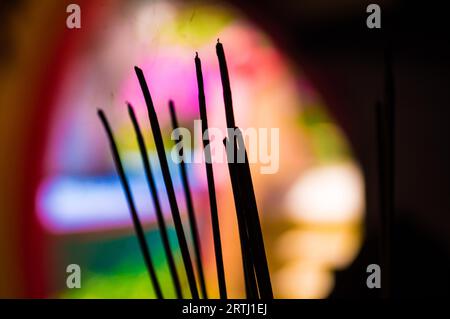 Joss Sticks werden vor einem bunten Hintergrund in einem chinesischen Tempel verbrannt. Rauch und Duft steigen in die Luft Stockfoto