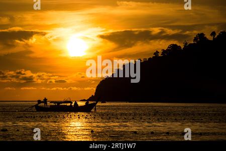 Blick auf den Sonnenuntergang vom Strand Pattaya in Ko Lipe, Thailand, zeigt ein Langboot, das vor der untergehenden Sonne fährt Stockfoto