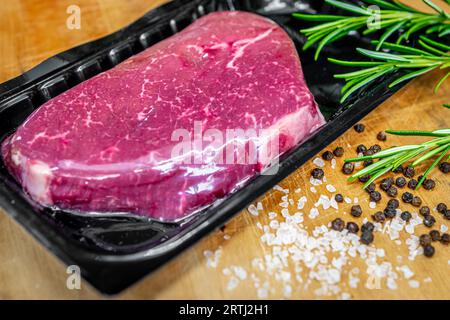 Vakuumverpacktes Rindersteak auf Holzschneidebrett mit Salz, Pfeffer und Rosmaringewürzen Stockfoto