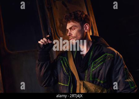 Der Mann überlebte nach der Apokalypse, indem er mit einer Waffe in der Nähe einer rostigen U-Bahn in dunklem Untergrund stand Stockfoto