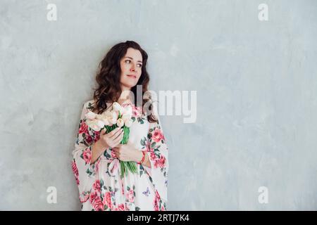 Eine Frau in einem Blumenkleid steht mit Tulpenblumen im Zimmer Stockfoto