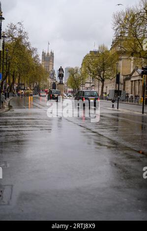 LONDON - 24. April 2023: Schwarze Taxis fahren an einem regnerischen Tag durch Whitehall, wobei die Houses of Parliament eine majestätische Kulisse bilden. Stockfoto