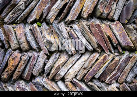 Abstrakte Steine, die in einem Fischgrätenmuster gelegt wurden, um eine Trockensteinmauer zu schaffen Stockfoto