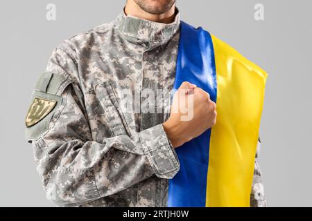 Männlicher Soldat mit ukrainischer Flagge auf grauem Hintergrund Stockfoto