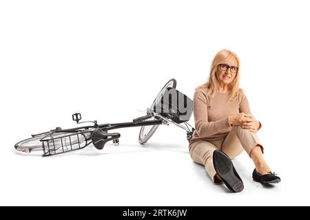Schmerzhafte Frau sitzt auf dem Boden neben einem Fahrrad und hält ihr Knie isoliert auf weißem Hintergrund Stockfoto
