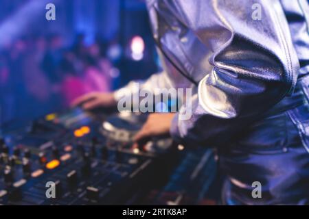 Ansicht von DJ-Mixer und Vinylplatte mit Kopfhörern auf einem Tisch mit weiblichem DJ, der auf der Bühne spielt und den Track während der Veranstaltung im Hintergrund mischt Stockfoto