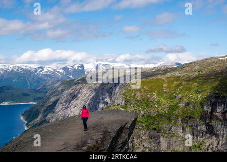 Eine Frau posiert auf Trolltunga (Trolls Zunge) mit Blick auf den Ringedalsvatnet Lake, in der Nähe von Tyssedal, Vestland, Norwegen. Stockfoto