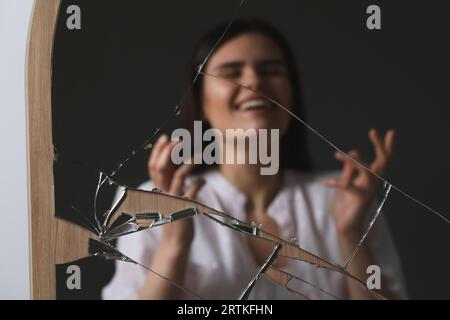 Verschwommenes Spiegelbild einer lächelnden Frau im gebrochenen Spiegel Stockfoto