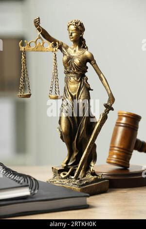 Figur der Lady Justice, Hammer und Notizbücher auf Holztisch im Innenbereich. Symbol der gerechten Behandlung nach dem Gesetz Stockfoto