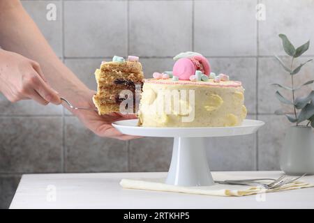 Frau, die ein Stück leckeren Kuchen am weißen Holztisch nimmt, Nahaufnahme Stockfoto