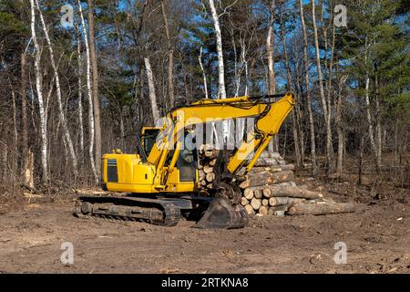 Gelber Bagger oder Bagger, der auf einem Baumstamm auf einer Baustelle für ein neues Zuhause auf dem Schmutz geparkt ist. Stockfoto