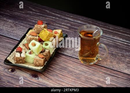Eine rechteckige schwarze Keramikplatte mit einer Auswahl an verschiedenen orientalischen Süßigkeiten und eine Tasse heißen Tee auf einem Holztisch. Nahaufnahme. Stockfoto