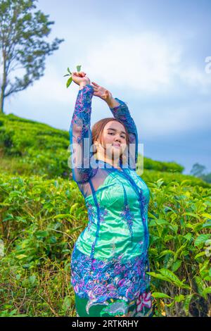 Ein Teegartenbauer posiert schön in der Mitte von grünen Teeblättern am Morgen Stockfoto