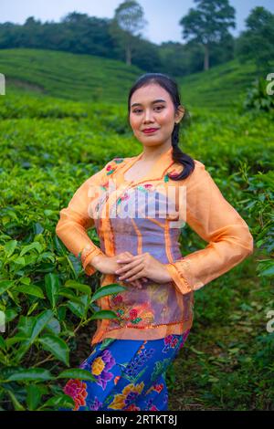 Ein Teeblätter-Bauer in einem orangen Kleid posiert morgens vor einem sehr schönen Teegarten Stockfoto