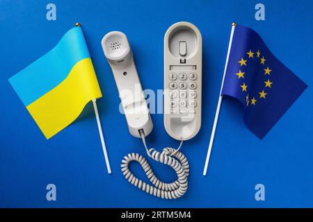 Draufsicht auf ein altes Telefon und zwei Flaggen auf blauem Hintergrund, Konzept zum Thema Telefongespräche zwischen der Ukraine und dem europäischen Unio Stockfoto