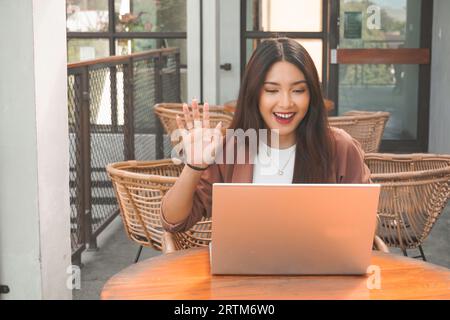 Junge asiatische Frau, die Videokonferenzen auf Laptop macht, während sie im Café sitzt und sich trifft Stockfoto