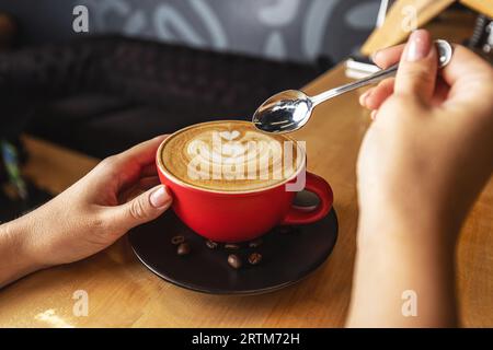 Hände einer Frau, die eine Tasse Cappuccino mit Kaffeekunst hält Stockfoto