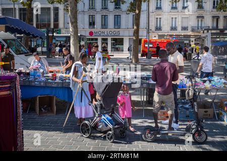 Eine Frau afrikanischer Herkunft steht mit ihrer kleinen Tochter und hält einen Besen und einen Kinderwagen, während sie die Stände vor dem Zentralmarkt (Marche d Stockfoto