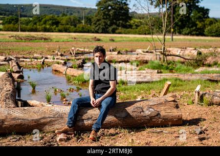 Ben Eardley, Project Manager National Trust, sitzt auf einem von Hunderten von Baumstämmen, die auf der neu gebildeten Hochwasserebene am Fluss aller auf dem National Trust Holnicote Estate, Exmoor, Somerset, aufgestellt wurden, wo der erste Versuch unternommen wurde, eine natürlichere, vielfältige und widerstandsfähige Feuchtgebiete und Landschaften im Vereinigten Königreich werden dazu beitragen, die Auswirkungen des Klimawandels wie Überschwemmungen und Dürren zu bekämpfen. Bilddatum: Mittwoch, 13. September 2023. Stockfoto