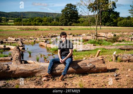 Ben Eardley, Project Manager National Trust, sitzt auf einem von Hunderten von Baumstämmen, die auf der neu gebildeten Hochwasserebene am Fluss aller auf dem National Trust Holnicote Estate, Exmoor, Somerset, aufgestellt wurden, wo der erste Versuch unternommen wurde, eine natürlichere, vielfältige und widerstandsfähige Feuchtgebiete und Landschaften im Vereinigten Königreich werden dazu beitragen, die Auswirkungen des Klimawandels wie Überschwemmungen und Dürren zu bekämpfen. Bilddatum: Mittwoch, 13. September 2023. Stockfoto