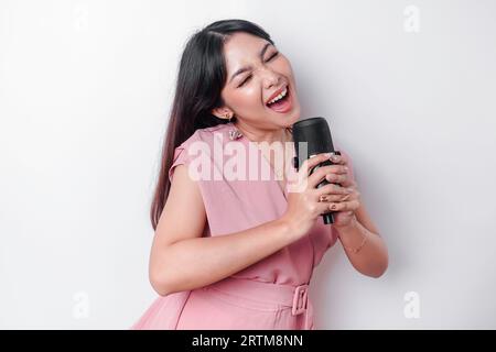 Porträt einer unbekümmerten asiatischen Frau, die Spaß mit Karaoke hat, im Mikrofon singt, während sie auf weißem Hintergrund steht Stockfoto