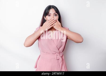 Hoppla! Überraschte junge asiatische Frau, die den Mund mit den Händen bedeckt und die Kamera anstarrt, während sie vor weißem Hintergrund steht Stockfoto