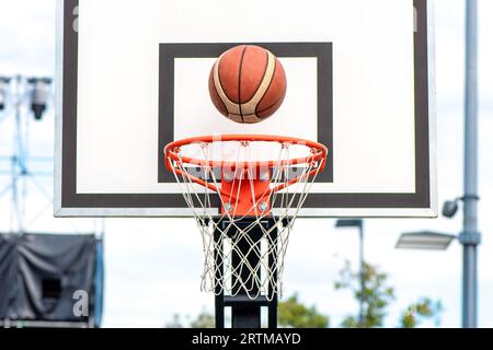 Basketballball tritt in den Korb ein. Vorderansicht von der Spielerposition, die auf der Straße auf dem Platz im Freien spielt Stockfoto