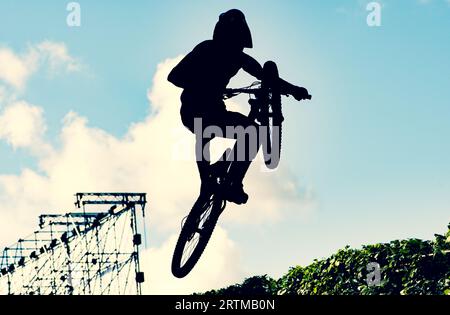 Silhouette eines Bikers, der mit einem bmx-Bike einen extrem schmutzigen Sprung gegen den Himmel macht Stockfoto