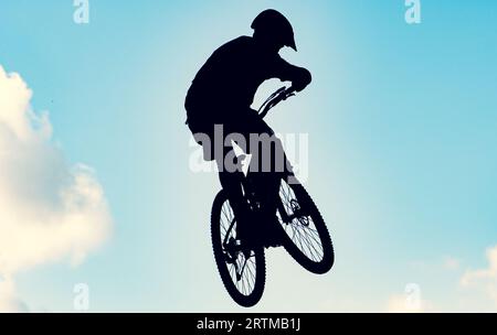 Silhouette eines Bikers, der mit einem bmx-Bike einen extrem schmutzigen Sprung gegen den Himmel macht Stockfoto