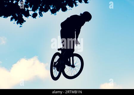 Silhouette eines Bikers, der mit einem bmx-Bike einen extrem schmutzigen Sprung gegen den Himmel macht Stockfoto