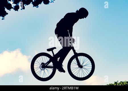 Silhouette eines Bikers, der mit einem bmx-Bike einen extrem schmutzigen Sprung gegen den Himmel macht Stockfoto