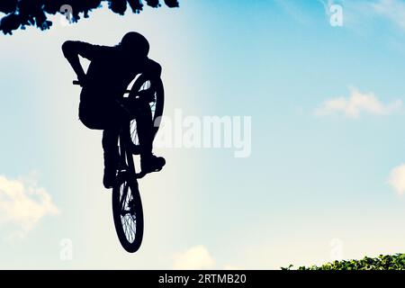 Silhouette eines Bikers, der mit einem bmx-Bike einen extrem schmutzigen Sprung gegen den Himmel macht Stockfoto