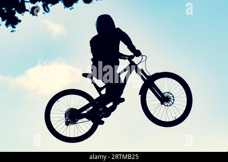 Silhouette eines Bikers, der mit einem bmx-Bike einen extrem schmutzigen Sprung gegen den Himmel macht Stockfoto