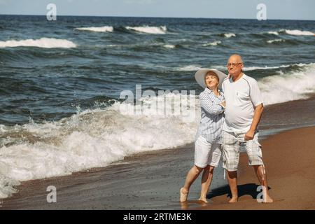 Ein älteres Paar steht am Strand am Meer, schaut auf die Wellen und entspannt sich. Vorderansicht. Stockfoto