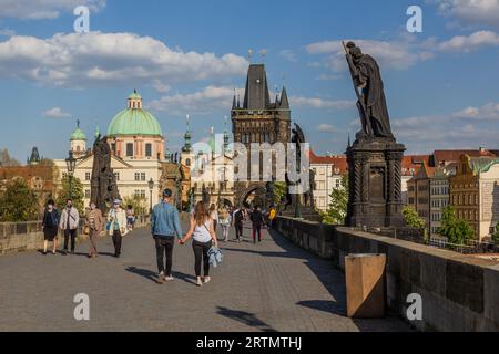 PRAG, TSCHECHIEN - 27. APRIL 2020: Maskentragende Menschen überqueren die Karlsbrücke in Prag während der COVID-19-Sperre in der Tschechischen Republik. Stockfoto