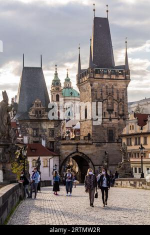 PRAG, TSCHECHIEN - 27. APRIL 2020: Maskentragende Menschen überqueren die Karlsbrücke in Prag während der COVID-19-Sperre in der Tschechischen Republik. Stockfoto