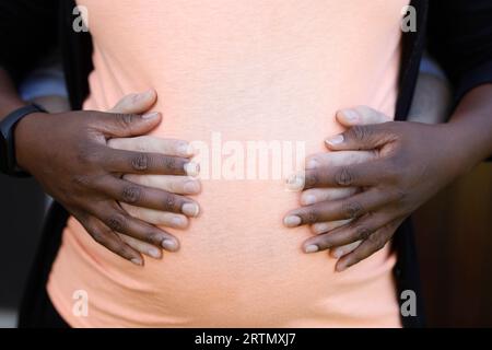 Weißer Mann umarmt schwangere schwarze Frau. Le Mesnil en Ouche, Frankreich. Nahaufnahme von Händen und Bauch Stockfoto
