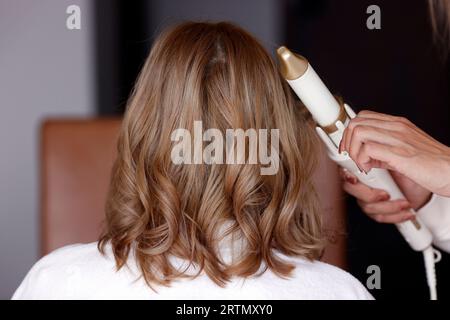 Hand des Friseurs, der lange und glänzend braune Haare einer jungen Frau im Schönheitssalon bürstet. Stockfoto