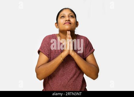 Eine junge Frau mit langen Haaren macht eine Bitte-Geste mit ihren Händen und schaut auf die Kamera. Sie trägt ein lässiges rotes Oberteil und Jeans. Stockfoto