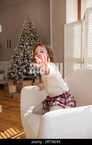 Unscharf verärgert kleines Mädchen will nicht fotografiert werden, wendet sich von der Kamera ab, bedeckt das Objektiv mit der Hand. Schädliches, freches Kind sitzt in wh Stockfoto