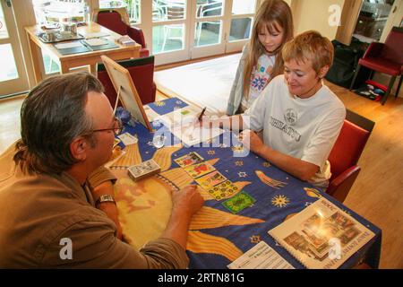 Eine sitzende Frau mit kurzen Haaren hat eine Tarotanzeige von einem Mann, während sie von einem kleinen Mädchen im Framlingham Crown Hotel und 2007 beobachtet wird Stockfoto