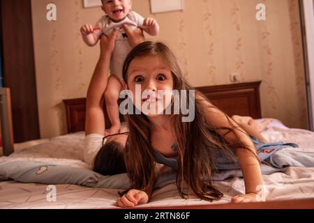 Ein kleines Mädchen im Teenageralter spielt auf dem Bett herum und hält ihre Zunge an die Kamera. Das Leben zu Hause, der Laystyle. Spaß am Morgen in der Familie. Nahaufnahme bestellung Stockfoto