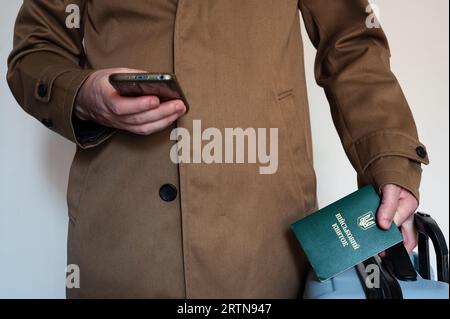 Übersetzung: "Militärische ID". Ziviler Mann hält Smartphone in einer Hand und Reisetasche und hat ukrainischen Militärausweis in der Manteltasche. Stockfoto