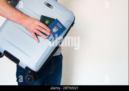 Mann in Jeans mit blauem Reisekoffer, ukrainischem Pass und grünem Dokument in der Hand Stockfoto