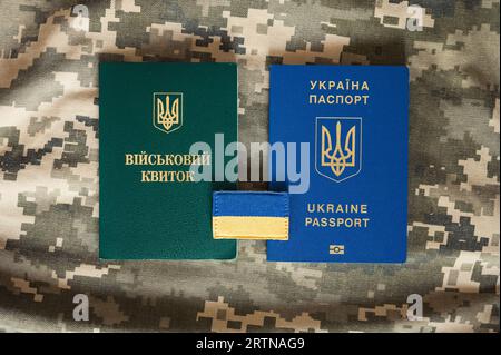 Übersetzung: "Militärische ID". Ukrainischer Pass und Armeedokument für Anfänger, Veteran, Soldat mit ukrainischer Flagge auf Tarnpixelhintergrund Stockfoto