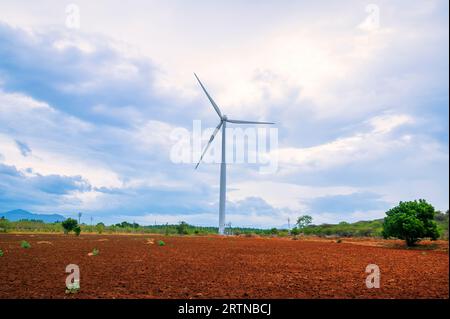 Windmühle – Windkraftanlage unterhalb des Berges auf dem Ackerland. Alternativer Energieerzeuger mit umweltfreundlichem Design. Windturbinen für Öko Stockfoto