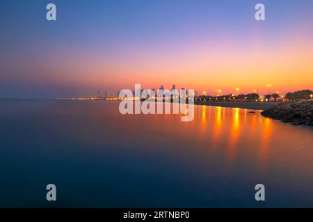 Blick auf die Skyline von Kuwait - mit dem bekanntesten Wahrzeichen von Kuwait City - bei Sonnenaufgang und Blick auf den Strand. Kuwaits Stadt ist von der Brücke mit Slow Shu abgehauen Stockfoto