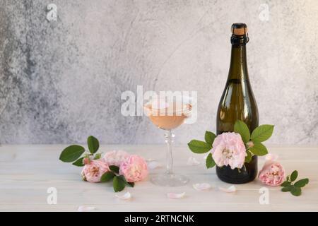 Glas rosa Champagner mit Rosenblüten auf hellgrauem Hintergrund Stockfoto